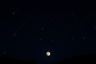A high-resolution image of a dark night sky with the Quadrantid meteor shower visible, with a full Wolf Moon hanging low in the horizon, and a few trees or hills in the foreground to give a sense of perspective.