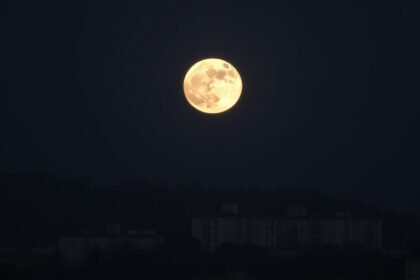 A high-quality image of the Wolf Moon supermoon rising over a cityscape or a natural landscape, with a clear view of the full moon and its surrounding environment.