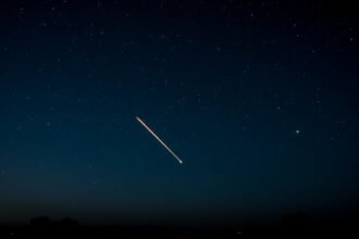 A stunning image of a meteor shower in the night sky, with a few meteors streaking across the stars, and a subtle hint of the Indian landscape in the foreground.