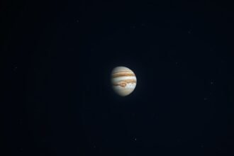 A high-quality image of the night sky with Jupiter prominently visible, with a few stars and constellations in the background, and a subtle moon glow.